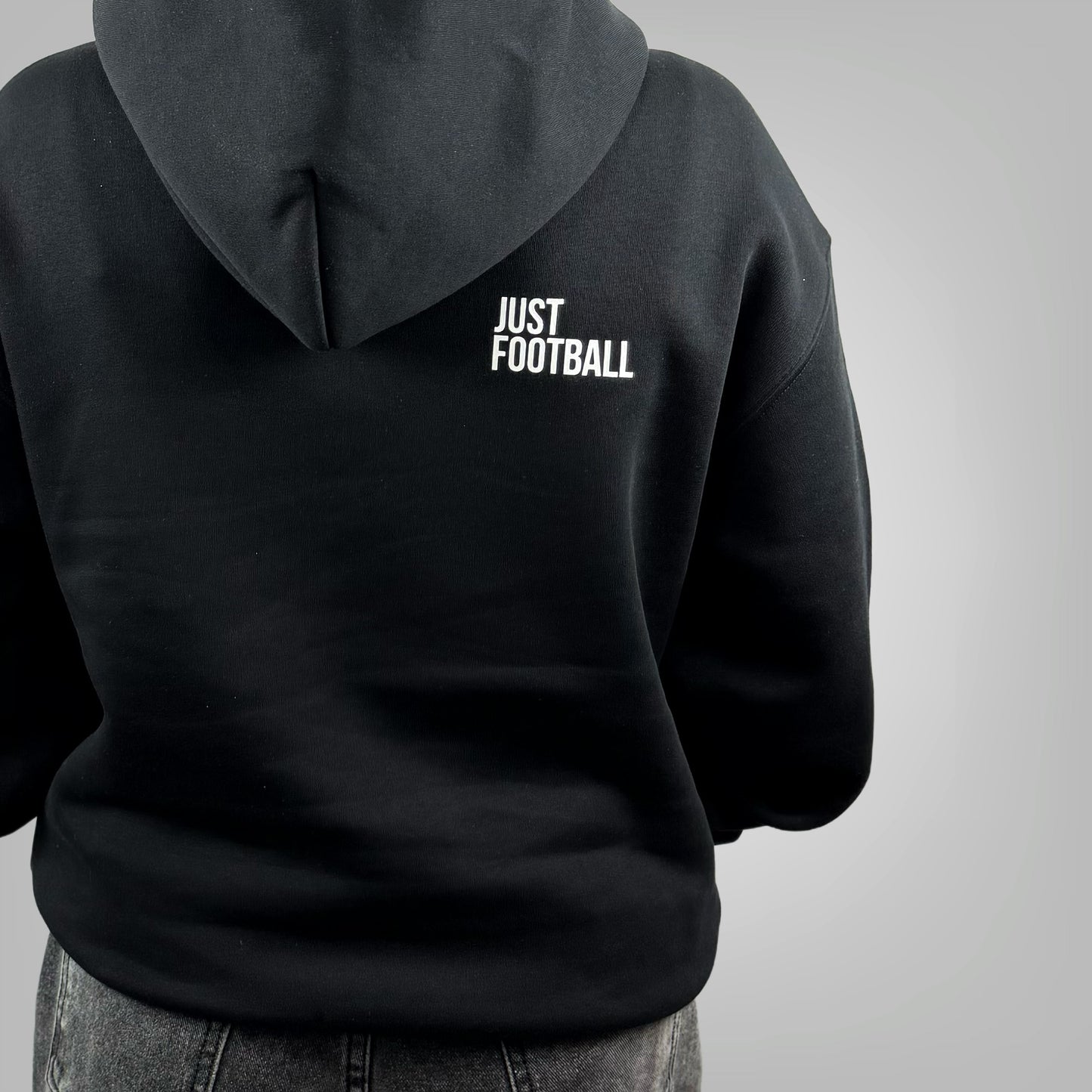 Close up of a female model wearing the ONETWENTI Its Just Football relaxed fit hoodie in black against a white background