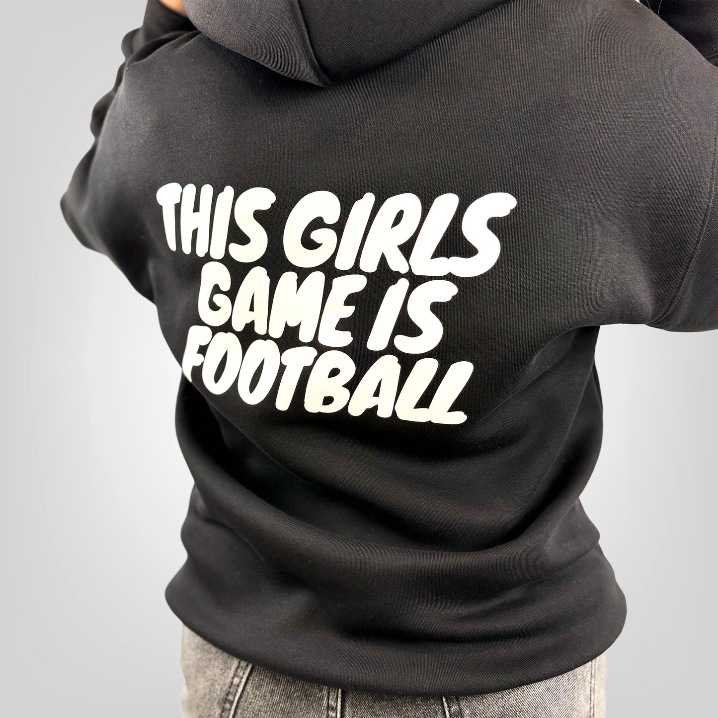 Close up view of a female model wearing the ONETWENTI This Girls Game Is Football relaxed fit hoodie in black.