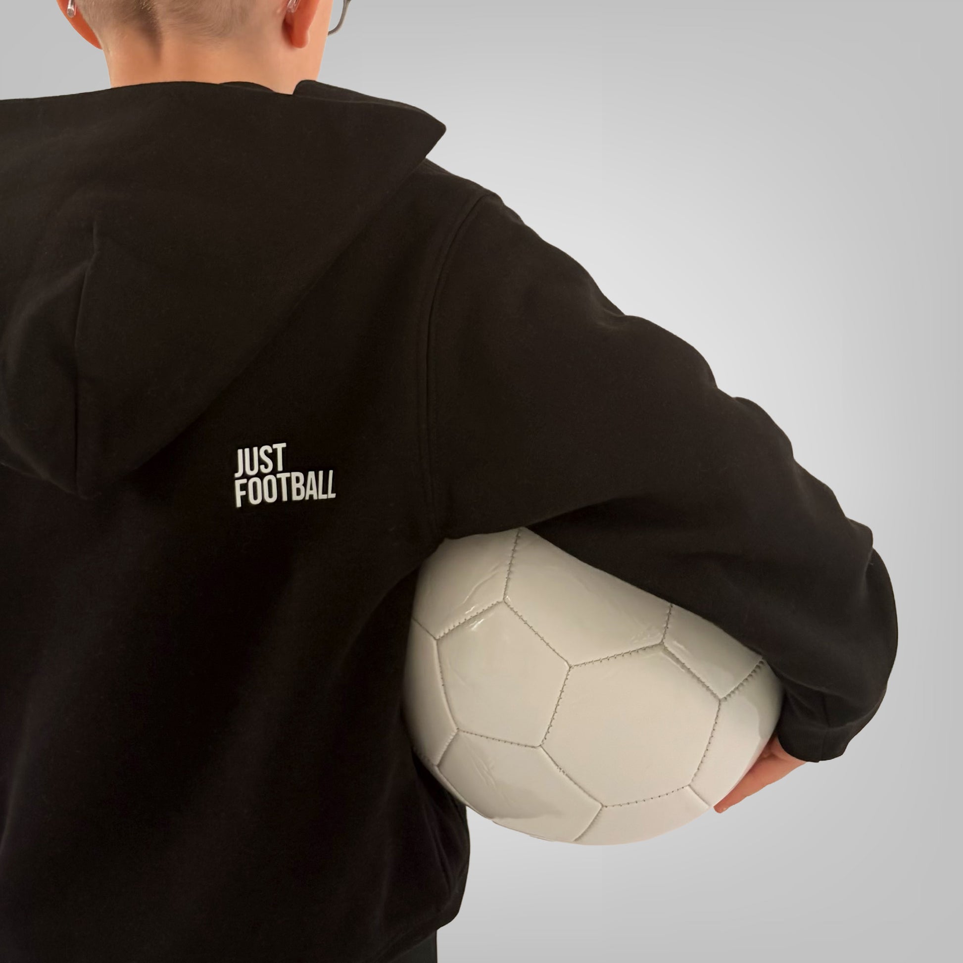 Close up of the back of black ONETWENTI Just Football hoodie worn by younger boy model with football