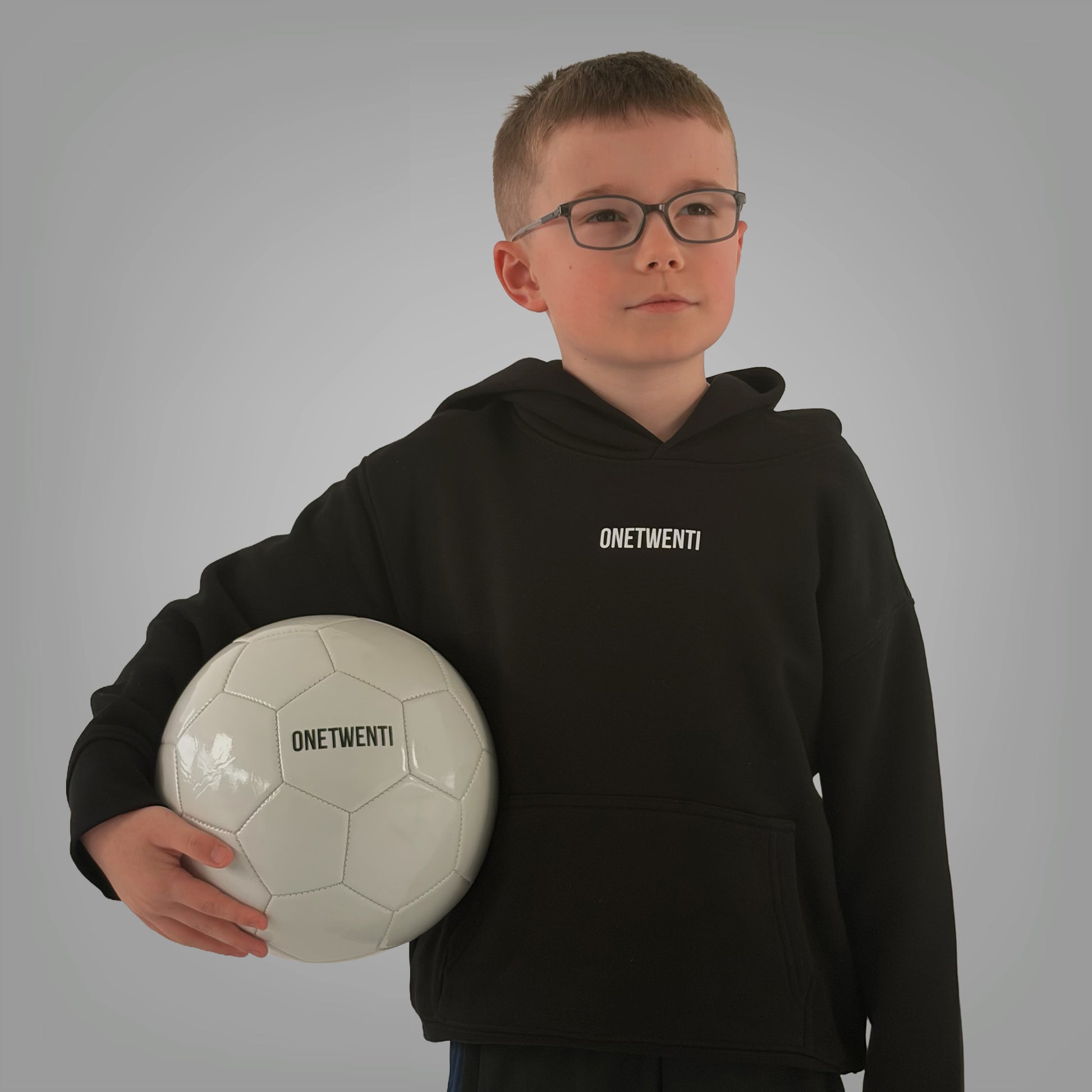 Front of black ONETWENTI Just Football hoodie worn by younger boy model with football