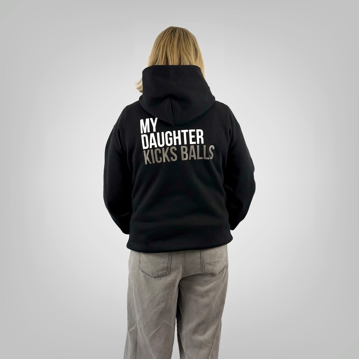 Back view of a female model wearing the ONETWENTI My Daughter Kicks Balls relaxed fit hoodie in black.