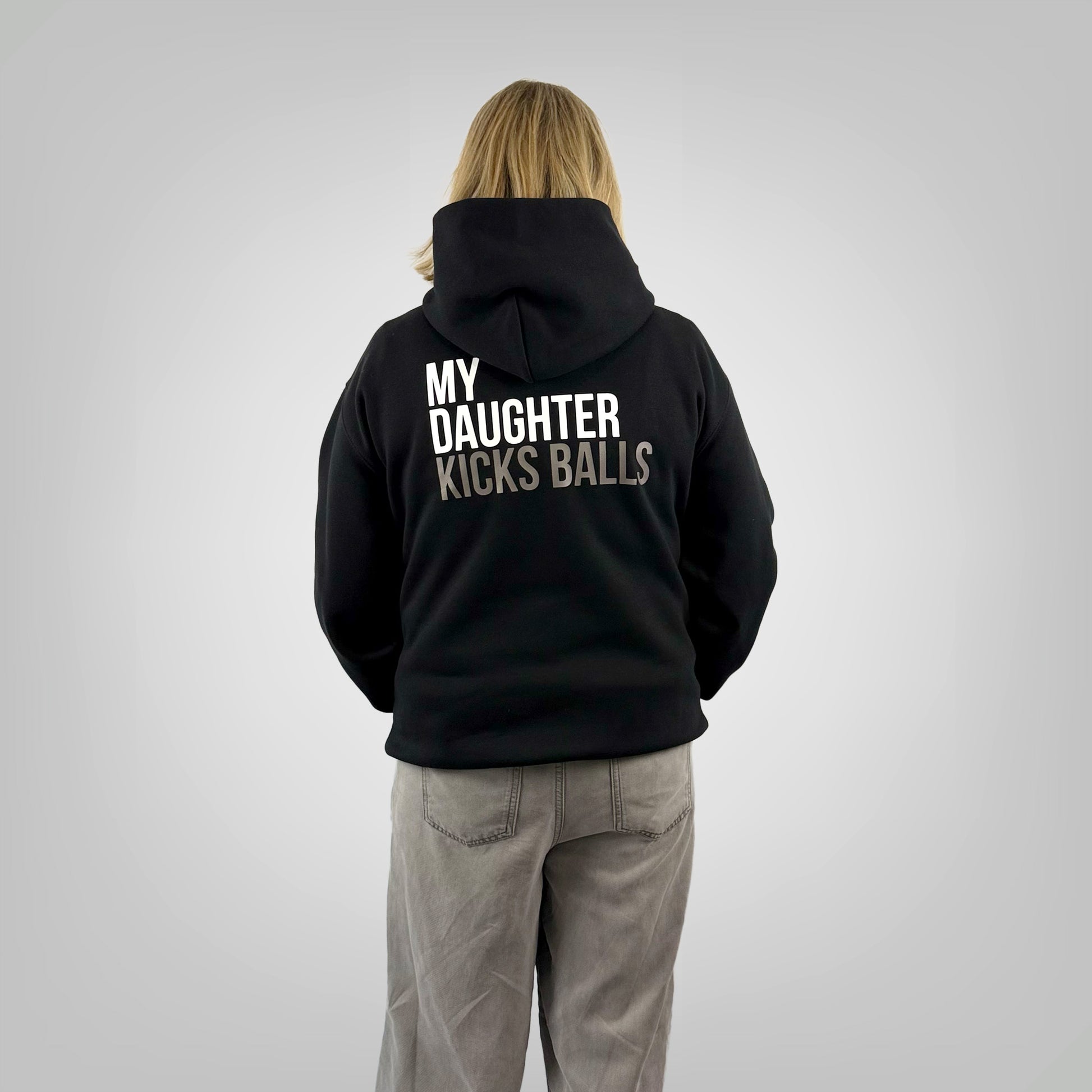 Back view of a female model wearing the ONETWENTI My Daughter Kicks Balls relaxed fit hoodie in black.