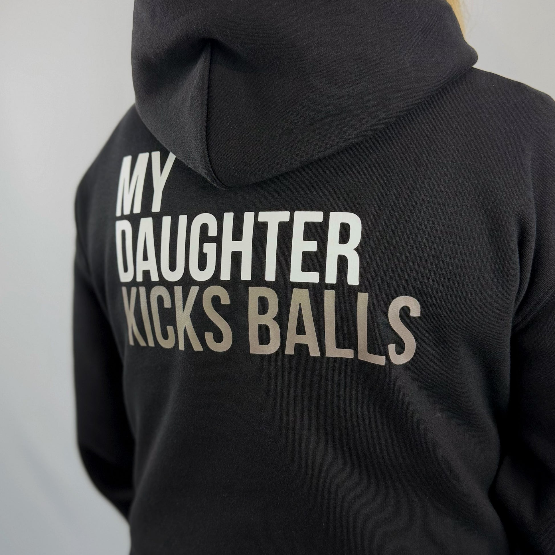 Close up view of a female model wearing the ONETWENTI My Daughter Kicks Balls relaxed fit hoodie in black.