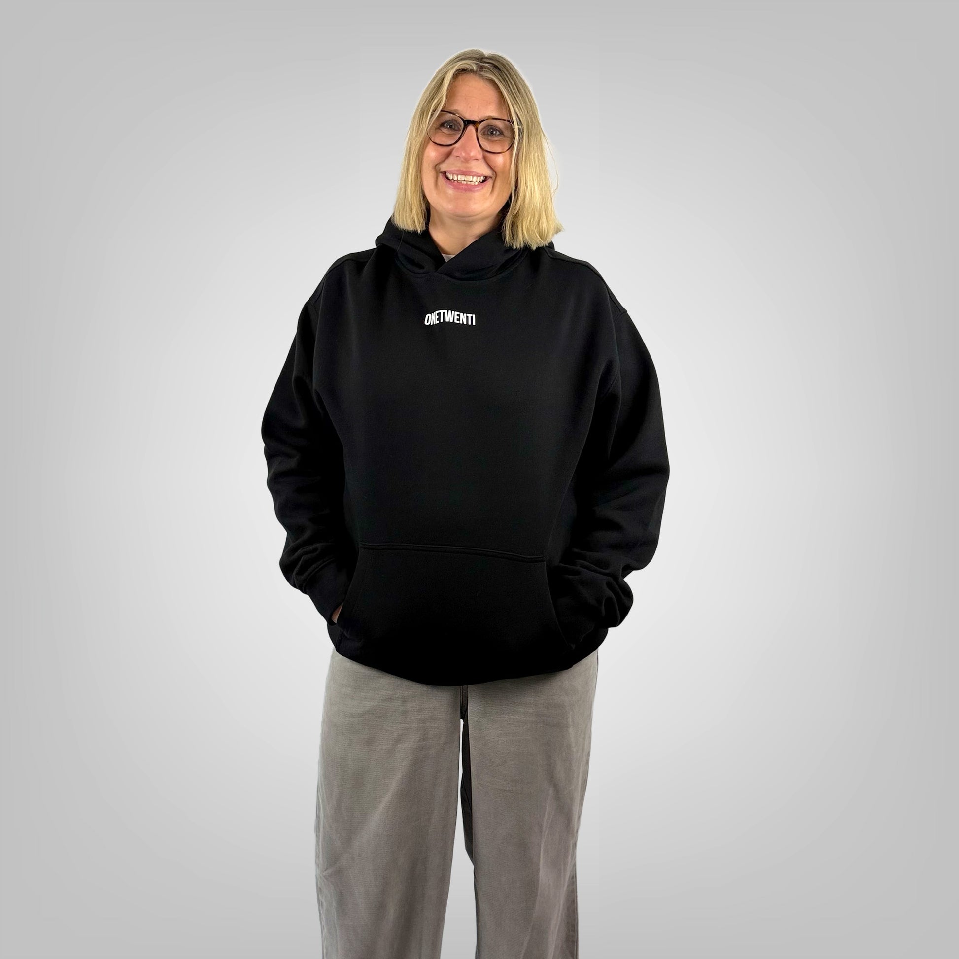Front view of a female model wearing the ONETWENTI My Daughter Kicks Balls relaxed fit hoodie in black.