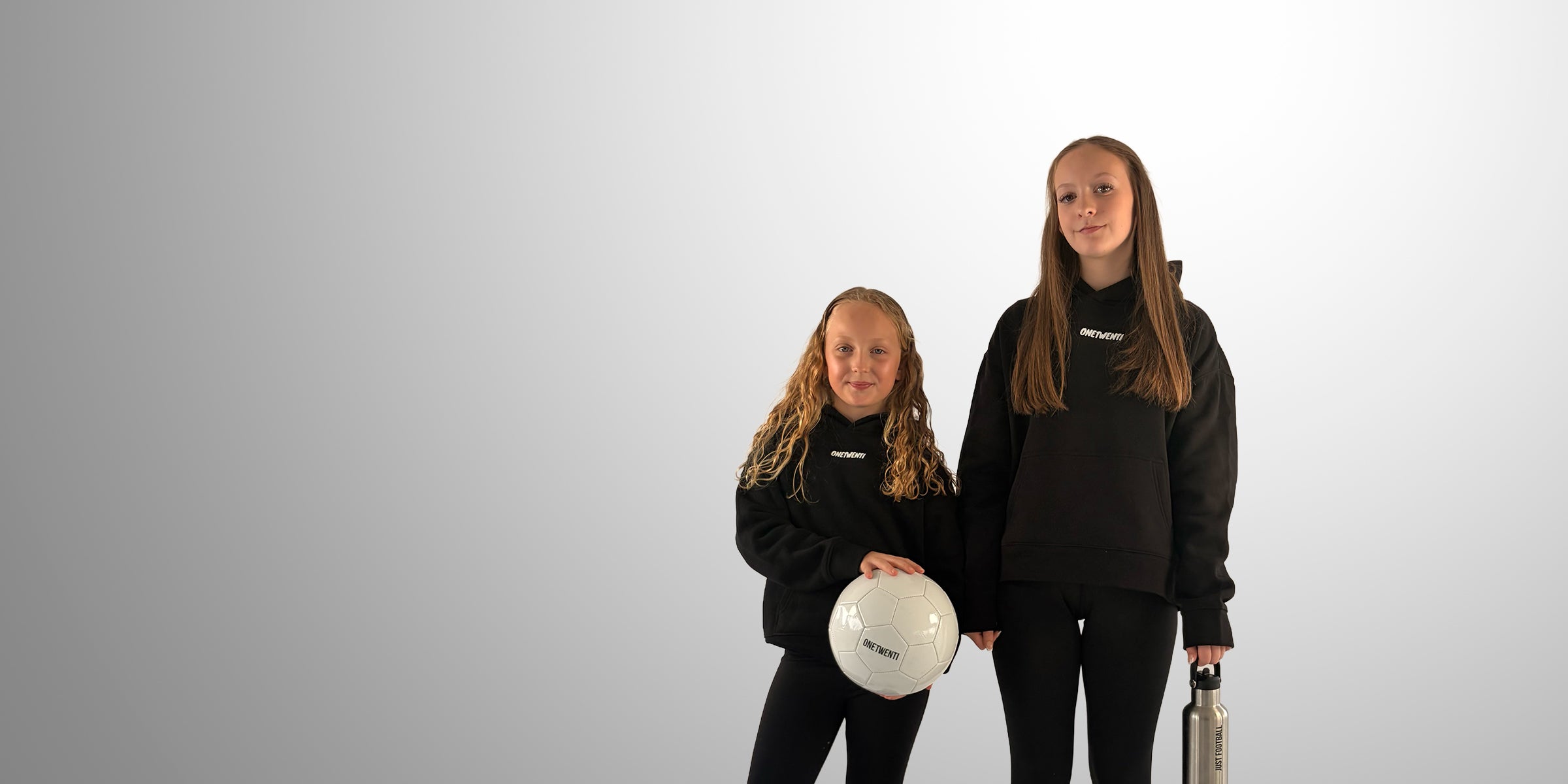 Two girls wearing black ONETWENTI hoodies with football, representing the 120 mindset in the women’s game