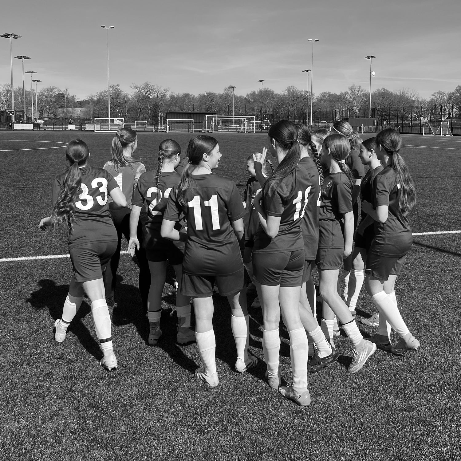 Girls football team huddle on pitch, representing 120FC community football