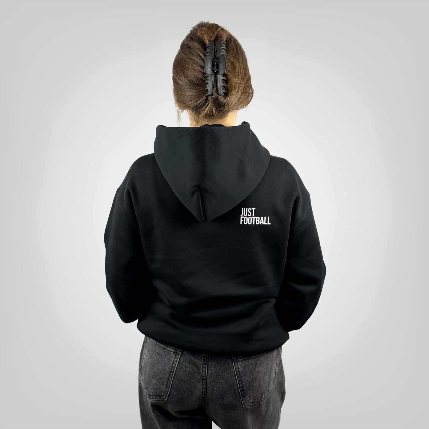 Person wearing a ONETWENTI black hoodie with 'Just Football' text on the back, standing against a plain background