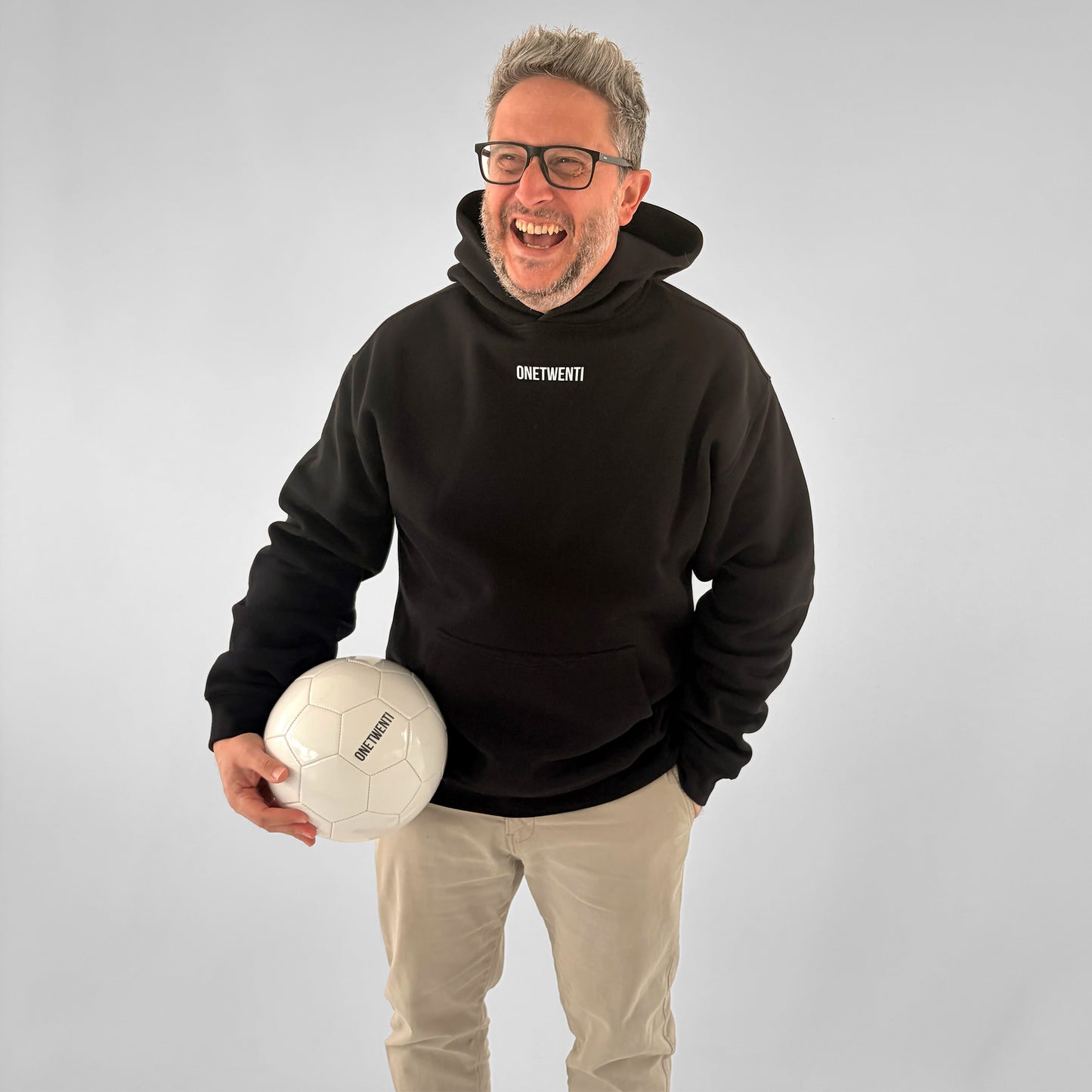 Front of black ONETWENTI My Daughter Kicks Balls hoodie worn by male model holding football