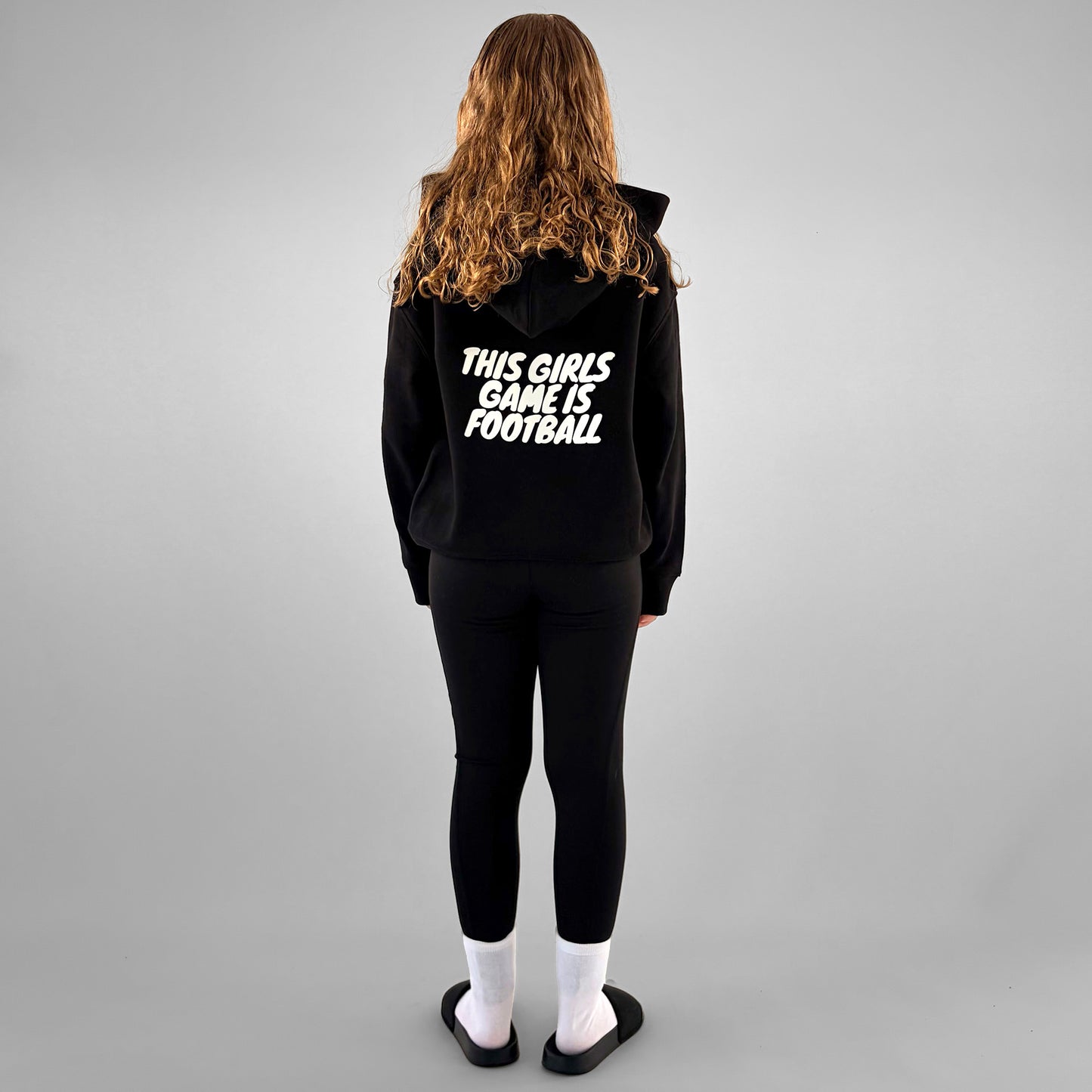 Full back of black ONETWENTI This Girl’s Game Is Football hoodie worn by younger model