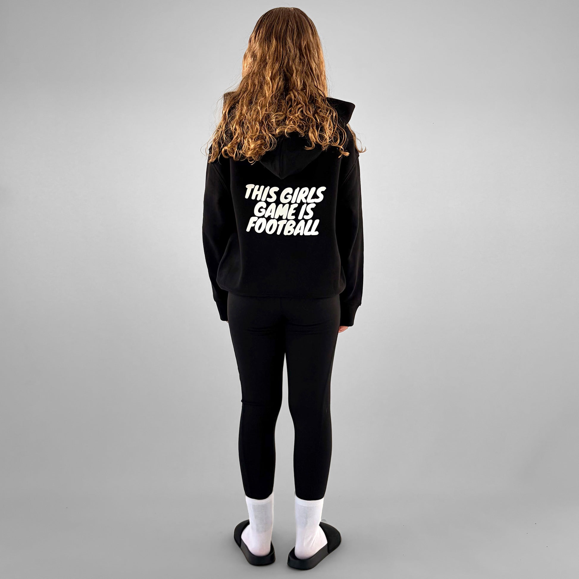 Full back of black ONETWENTI This Girl’s Game Is Football hoodie worn by younger model