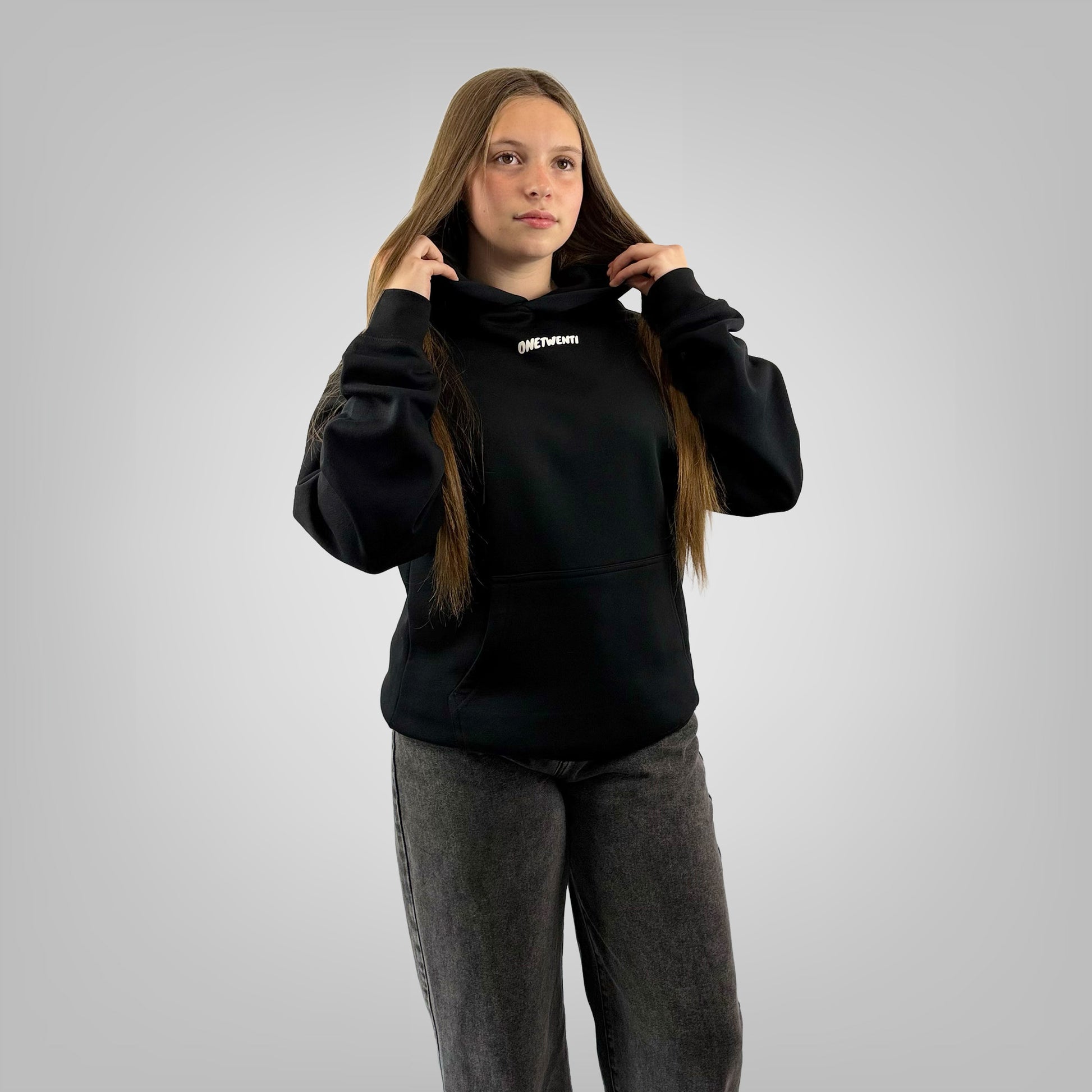 Female model wearing the ONETWENTI This Girls Game Is Football relaxed fit hoodie in black.